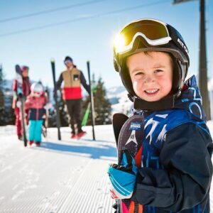 child holding skis and family behind in the snow