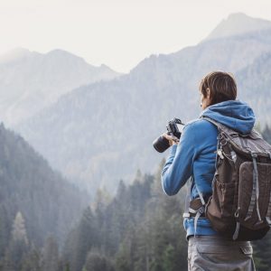 Mann mit Rucksack oben auf dem Berg mit einer Fotokamera
