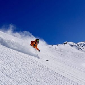 Man wearing an orange jacket skiing down in a powder snow