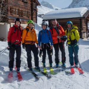 five skiers with colorful ski clothes some wood houses behind